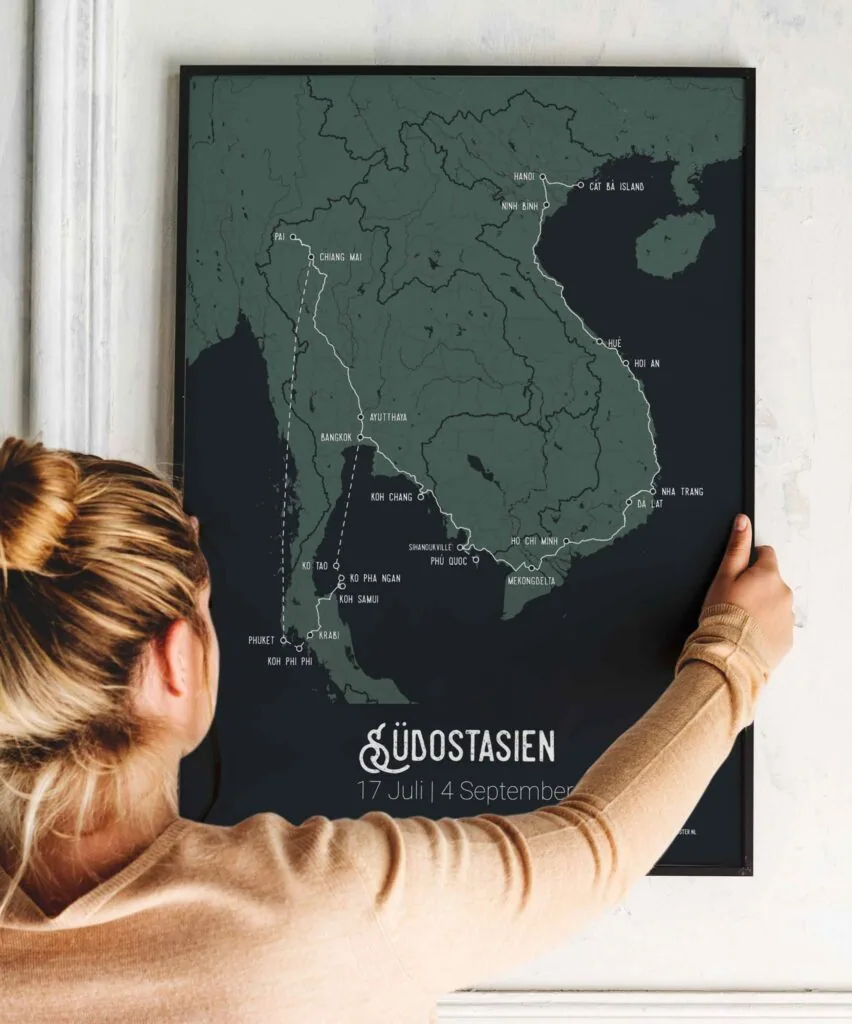 Vrouw hangt een ingelijste reisposter van Zuidoost-Azië aan een witte muur